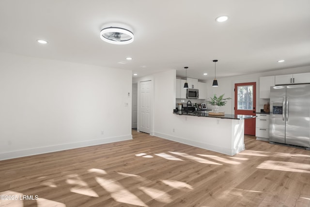 kitchen with appliances with stainless steel finishes, pendant lighting, white cabinetry, kitchen peninsula, and light wood-type flooring