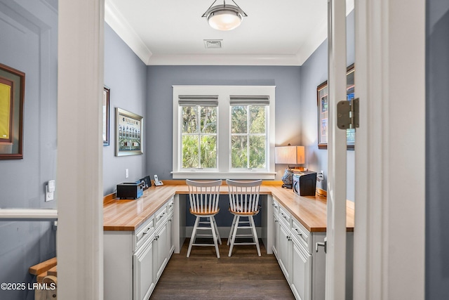 office with visible vents, dark wood finished floors, built in desk, and ornamental molding