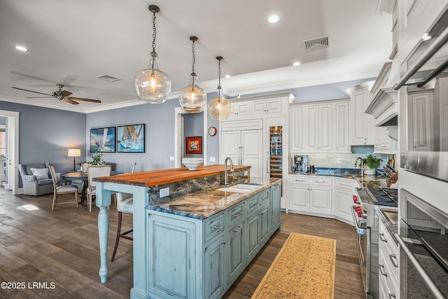 kitchen with visible vents, high quality appliances, white cabinets, hanging light fixtures, and a center island with sink