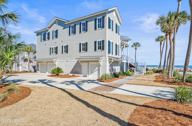 coastal home featuring a garage, a water view, stairs, driveway, and stucco siding