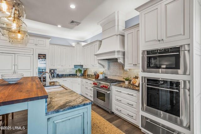 kitchen with wood counters, visible vents, hanging light fixtures, appliances with stainless steel finishes, and an island with sink