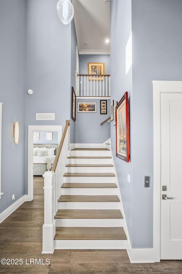 staircase with ornamental molding, a towering ceiling, baseboards, and wood finished floors