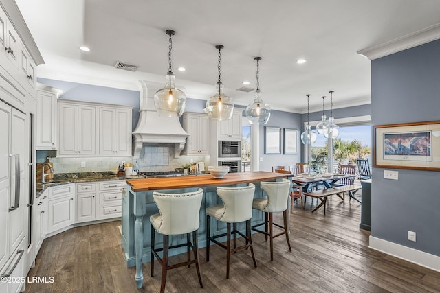 kitchen featuring butcher block counters, white cabinetry, a breakfast bar area, and decorative light fixtures