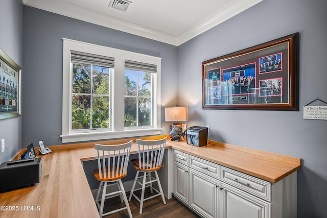 office space featuring ornamental molding, dark wood-type flooring, built in study area, and visible vents