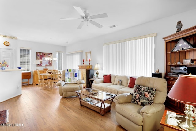 living area with ceiling fan with notable chandelier, light wood-style floors, and visible vents