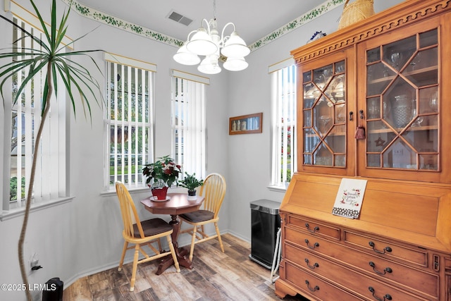 dining room with a wealth of natural light, visible vents, an inviting chandelier, and wood finished floors