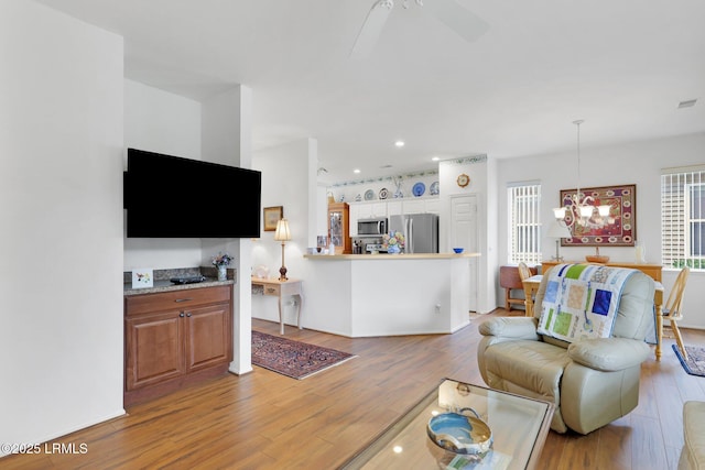 living room with ceiling fan with notable chandelier and light wood-style floors