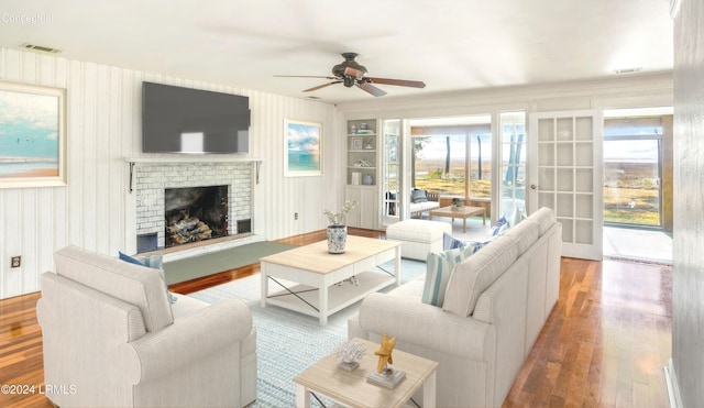 living room with ceiling fan, hardwood / wood-style floors, a fireplace, built in shelves, and french doors