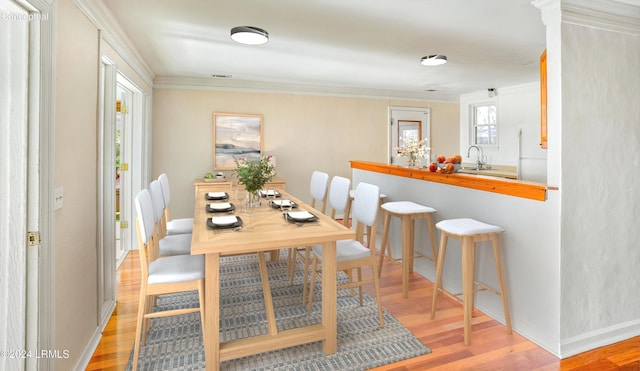 dining room with ornamental molding, sink, and light hardwood / wood-style floors