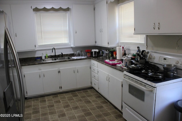 kitchen with white range with electric stovetop, white cabinets, dark countertops, freestanding refrigerator, and a sink