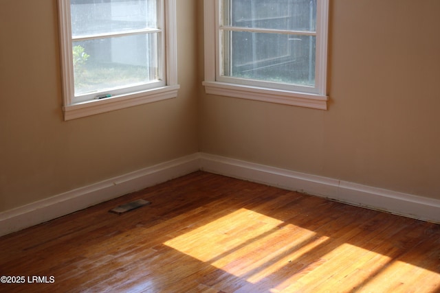 unfurnished room with wood finished floors, visible vents, and baseboards