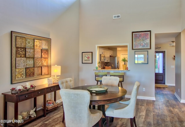 dining area featuring dark wood-style floors, a high ceiling, and baseboards