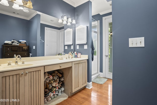bathroom featuring wood-type flooring, a stall shower, ornamental molding, and a sink