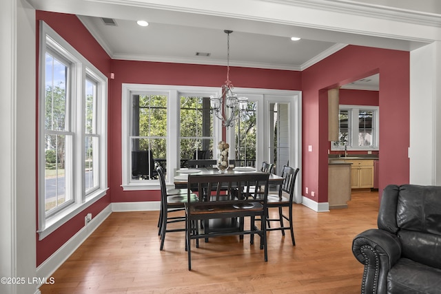 dining area with light wood-style floors, a healthy amount of sunlight, an inviting chandelier, and crown molding