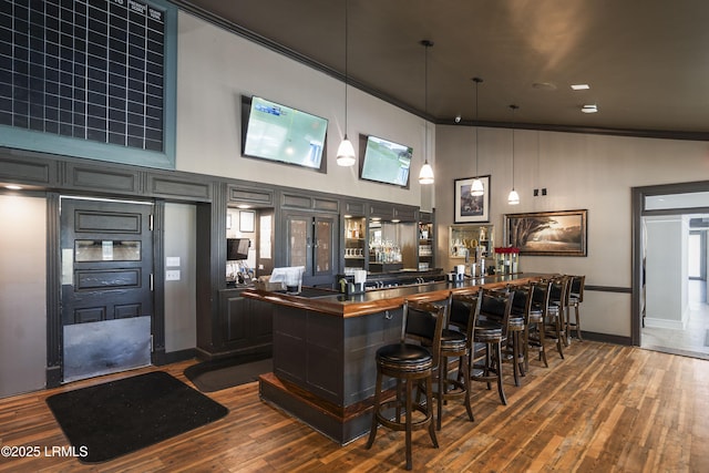 bar with a community bar, a towering ceiling, baseboards, and dark wood-style floors