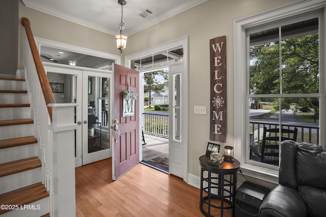 entrance foyer featuring stairway, crown molding, light wood-type flooring, and a healthy amount of sunlight