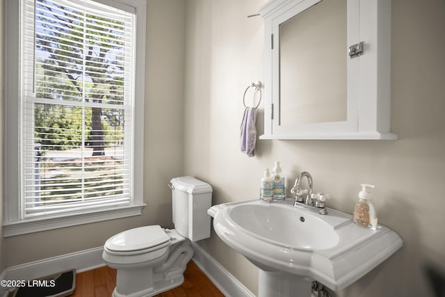 half bath featuring toilet, baseboards, a sink, and wood finished floors