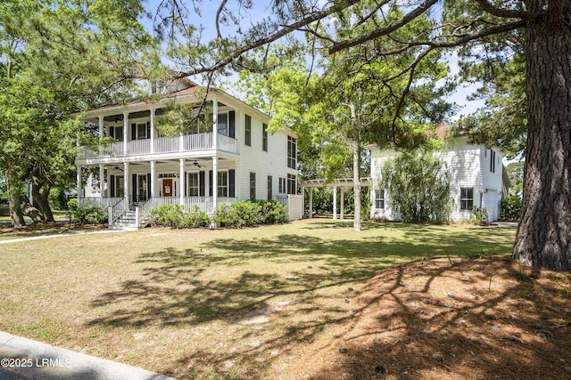 exterior space featuring covered porch, a front lawn, ceiling fan, and a balcony