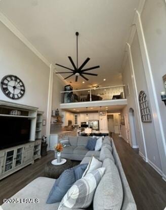 living room featuring baseboards, a towering ceiling, ornamental molding, wood finished floors, and an inviting chandelier