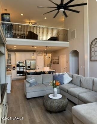 living area featuring arched walkways, visible vents, dark wood-style flooring, and a towering ceiling