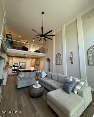 living room featuring a towering ceiling, crown molding, arched walkways, and wood finished floors