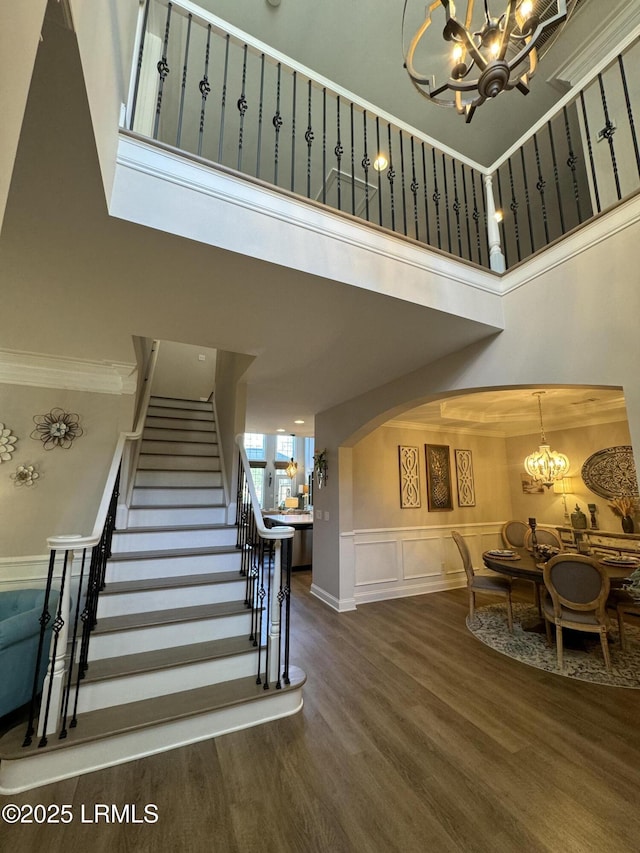 staircase with a chandelier, a decorative wall, a high ceiling, wood finished floors, and wainscoting