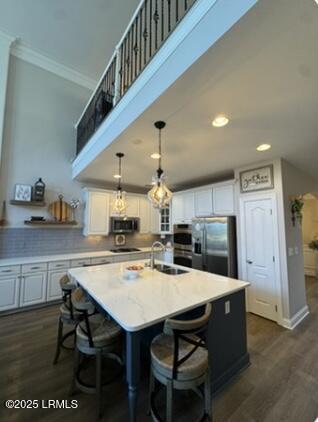 kitchen with dark wood finished floors, stainless steel appliances, white cabinets, a kitchen island with sink, and a sink