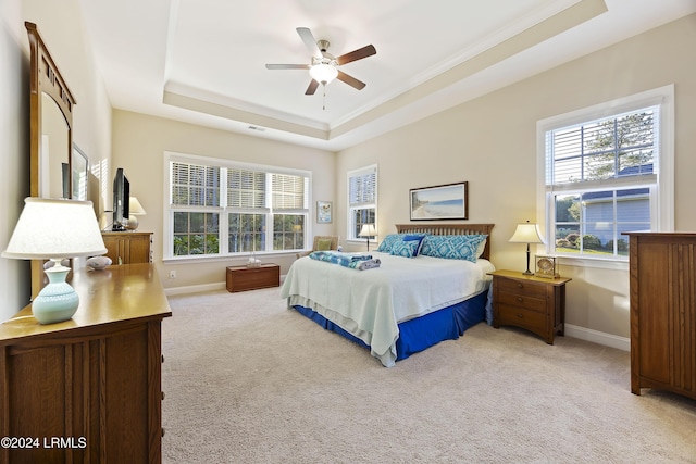 bedroom featuring light carpet, a tray ceiling, ornamental molding, and ceiling fan