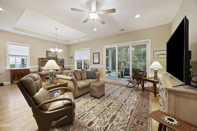 living room featuring ceiling fan with notable chandelier, light hardwood / wood-style flooring, and a raised ceiling