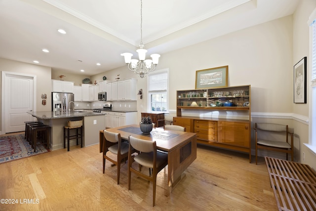 dining room with a notable chandelier, sink, light hardwood / wood-style floors, and a raised ceiling