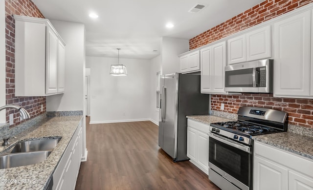 kitchen with appliances with stainless steel finishes, pendant lighting, white cabinetry, sink, and light stone counters