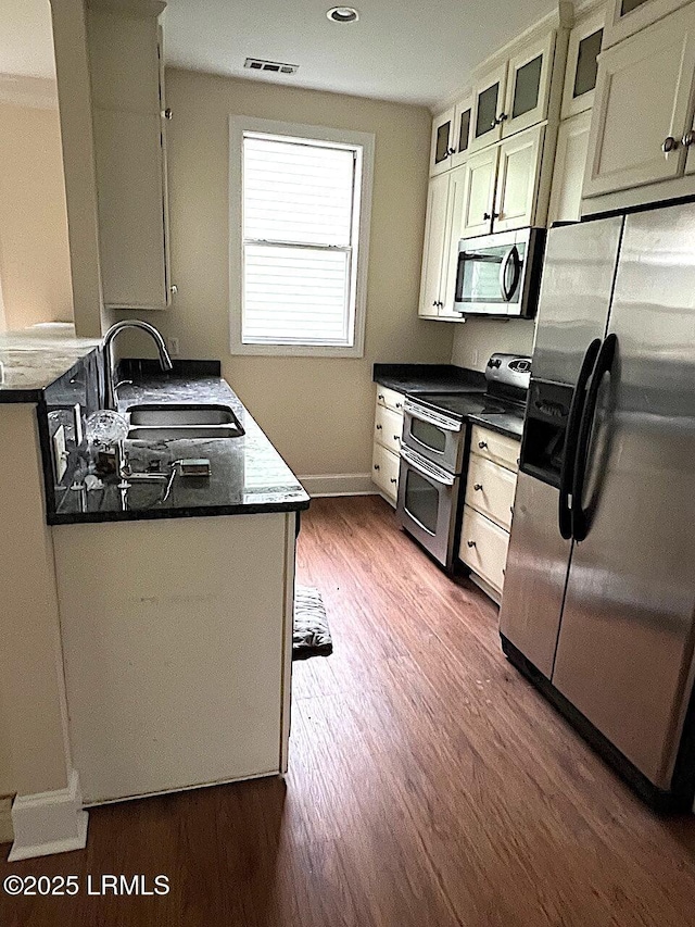 kitchen featuring visible vents, dark wood finished floors, glass insert cabinets, appliances with stainless steel finishes, and a sink