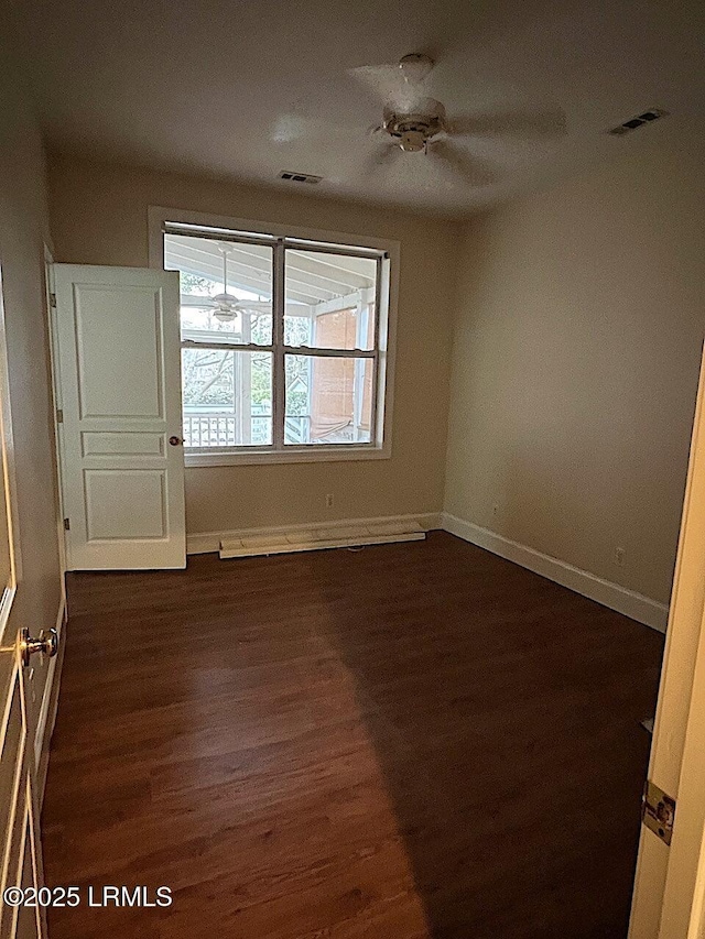 spare room featuring dark wood-style floors, a baseboard heating unit, visible vents, and baseboards