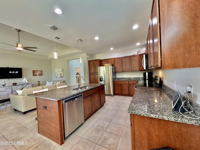 kitchen with brown cabinetry, visible vents, dark stone countertops, a sink, and stainless steel appliances