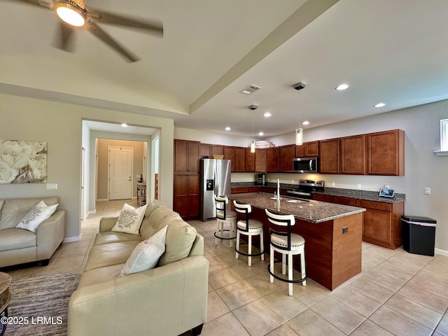 kitchen featuring light tile patterned floors, a ceiling fan, appliances with stainless steel finishes, open floor plan, and a breakfast bar area