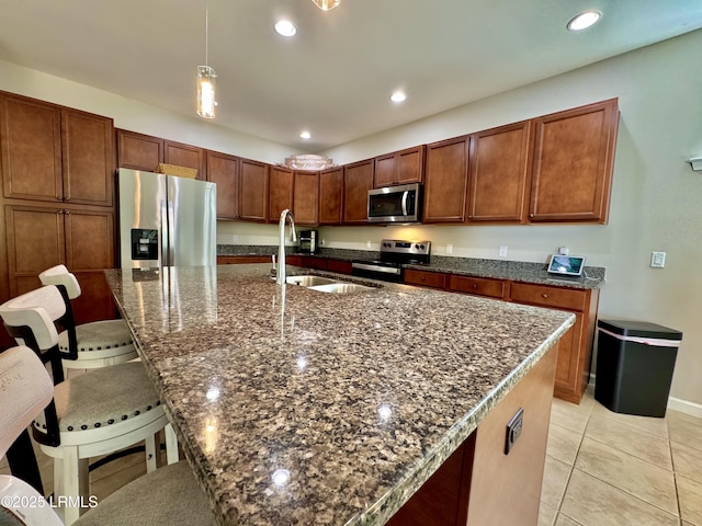 kitchen featuring recessed lighting, dark stone countertops, appliances with stainless steel finishes, a sink, and a breakfast bar area