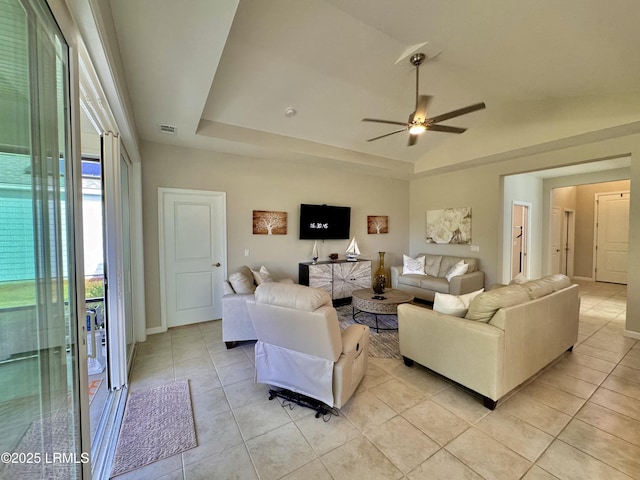 living area featuring a tray ceiling, light tile patterned flooring, a ceiling fan, and visible vents