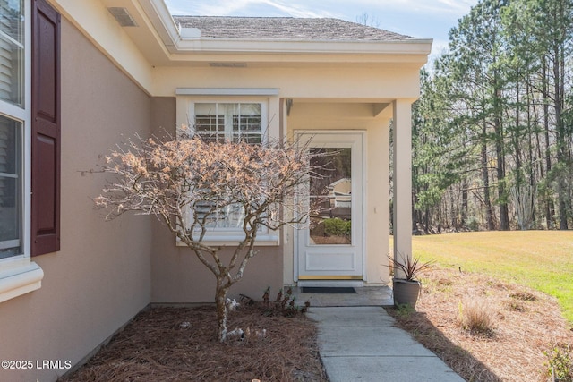 entrance to property featuring a shingled roof, a lawn, and stucco siding