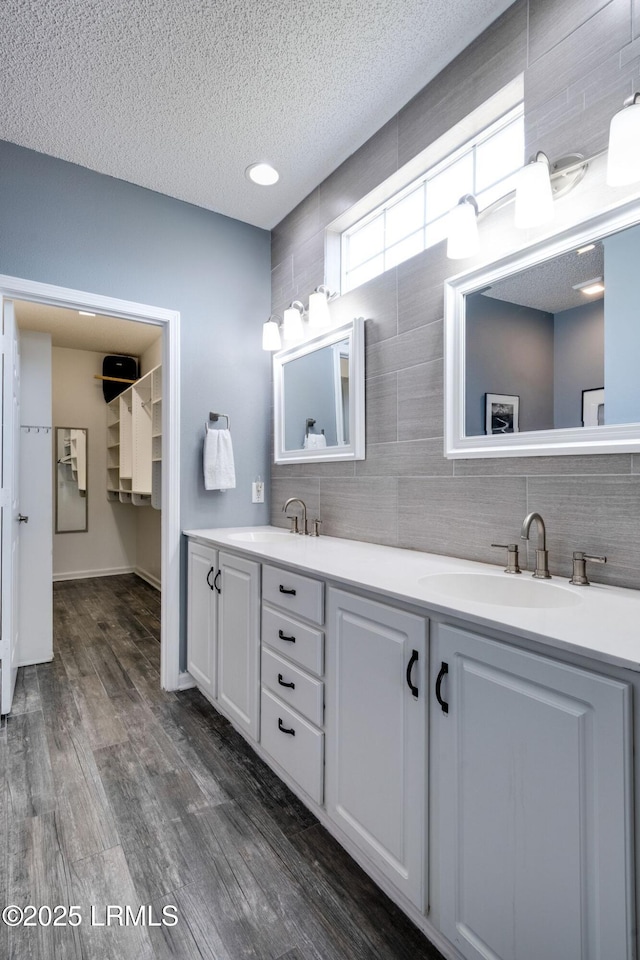 bathroom with a textured ceiling, double vanity, wood finished floors, and a sink