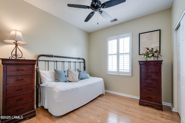 bedroom featuring visible vents, light wood-style flooring, a textured ceiling, and baseboards