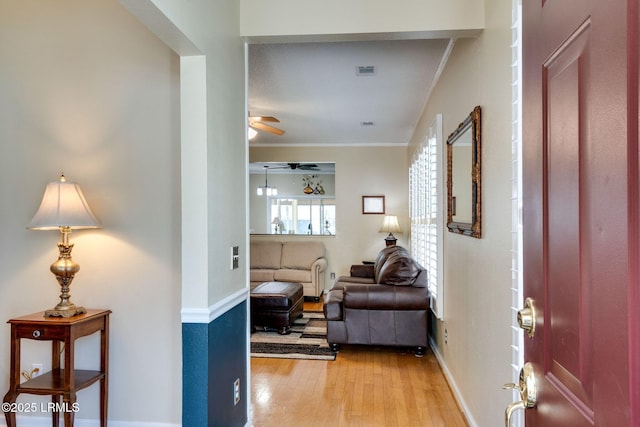 corridor with baseboards, visible vents, light wood finished floors, and ornamental molding