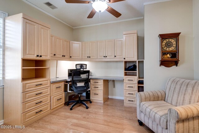 home office featuring a ceiling fan, visible vents, light wood-style flooring, ornamental molding, and built in desk