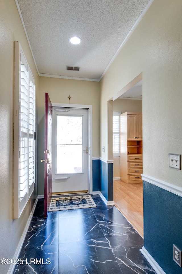 doorway to outside with visible vents, a textured ceiling, a textured wall, and ornamental molding