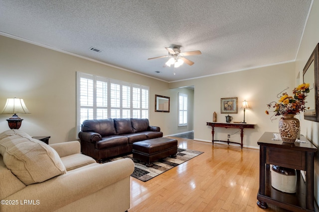 living area with visible vents, ceiling fan, ornamental molding, light wood-style floors, and a textured ceiling