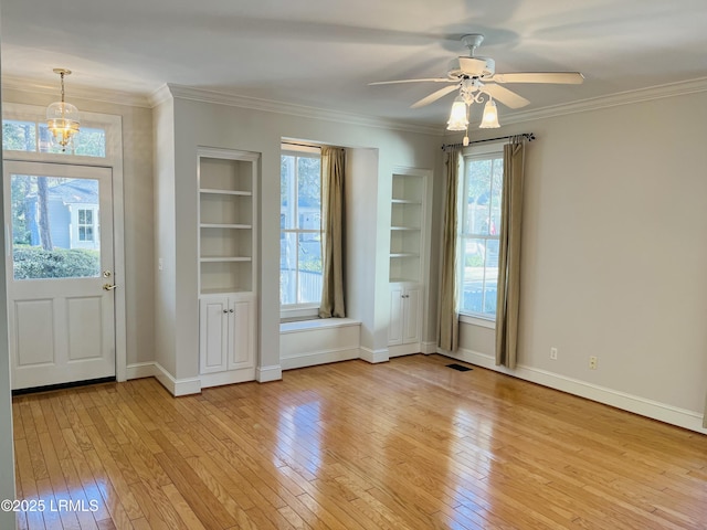 interior space with built in shelves, a healthy amount of sunlight, ornamental molding, and light wood-type flooring