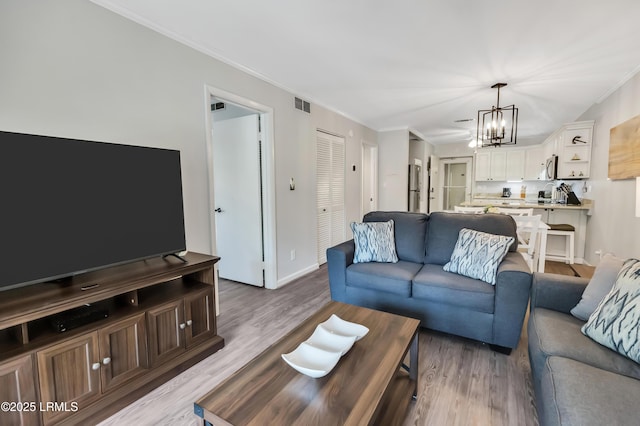 living room featuring a notable chandelier, ornamental molding, and light hardwood / wood-style floors