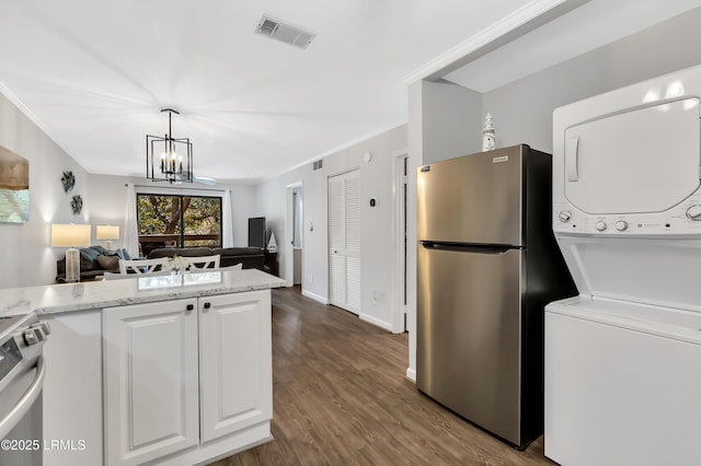 kitchen featuring stainless steel appliances, white cabinetry, stacked washer and clothes dryer, and crown molding