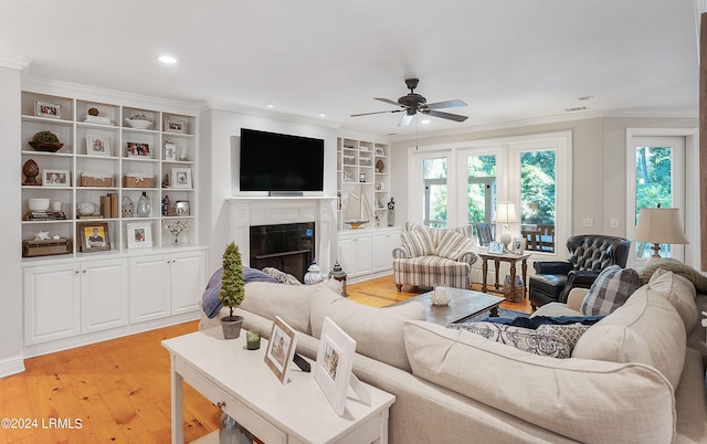 living room with ceiling fan, ornamental molding, a tiled fireplace, and light hardwood / wood-style flooring