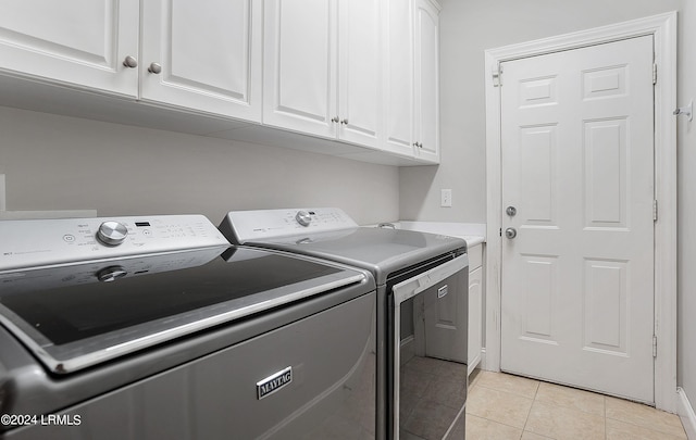 clothes washing area with cabinets, light tile patterned floors, and washer and clothes dryer