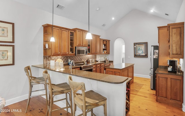 kitchen featuring appliances with stainless steel finishes, pendant lighting, high vaulted ceiling, tasteful backsplash, and kitchen peninsula